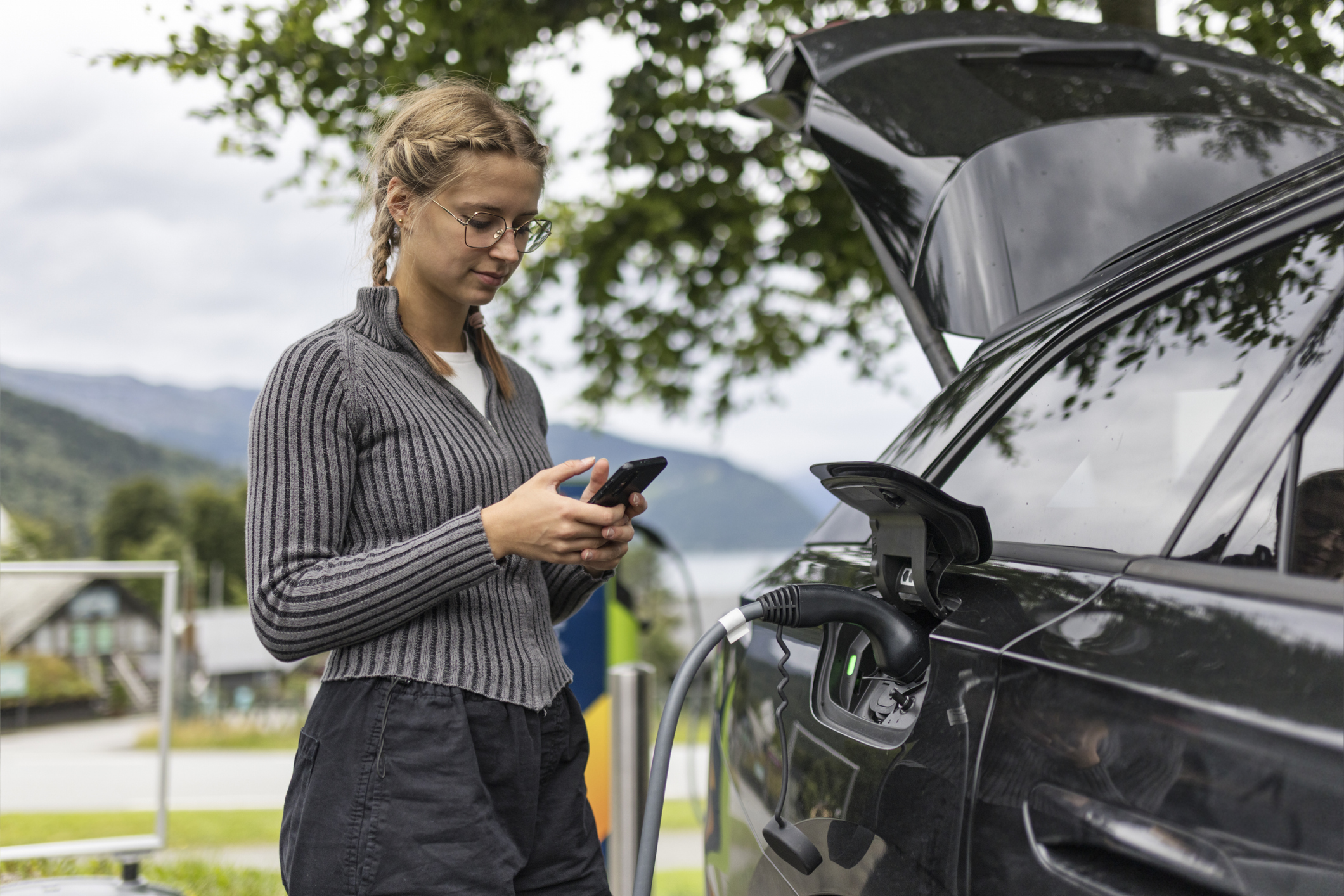 Young woman using smartphone app to control electric vehicle charging at urban station